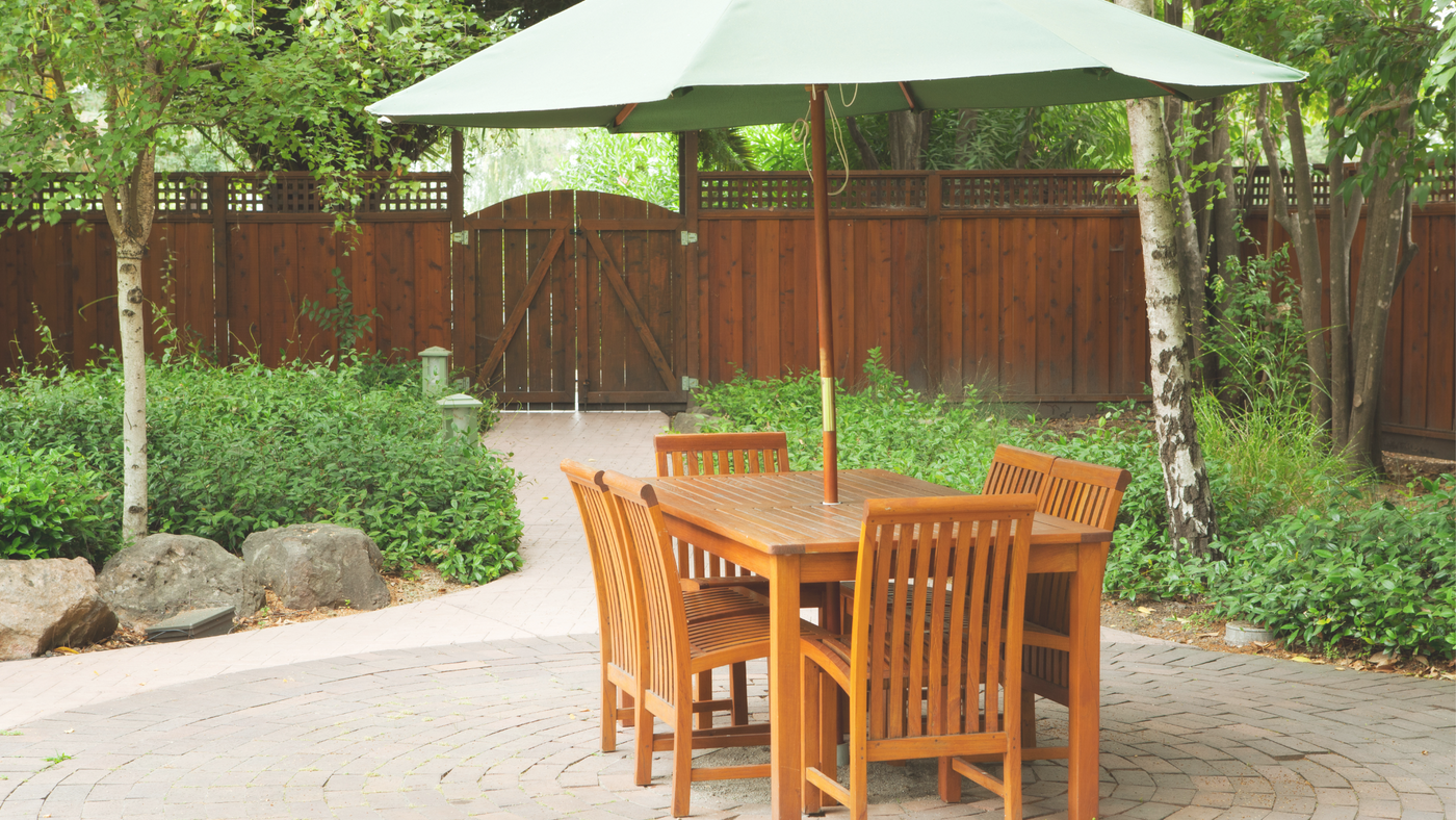 A freshly-oiled timber outdoor dining setting with an umbrella in a garden setting